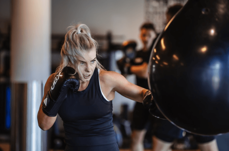 Woman punching a boxing bag with focus and intensity during a UBX training session.