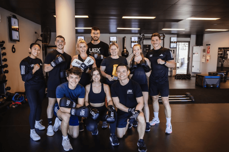 UBX members train together in a high-energy group workout, throwing punches and performing strength exercises to motivational music in a dynamic gym environment.